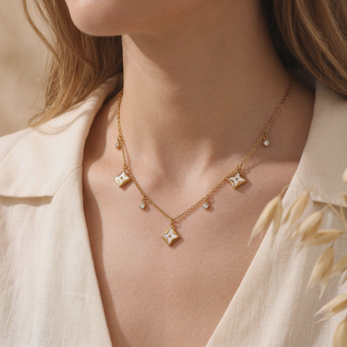 Gold-tone necklace with white-inlaid star pendants and dangling clear accents worn on a woman's neck