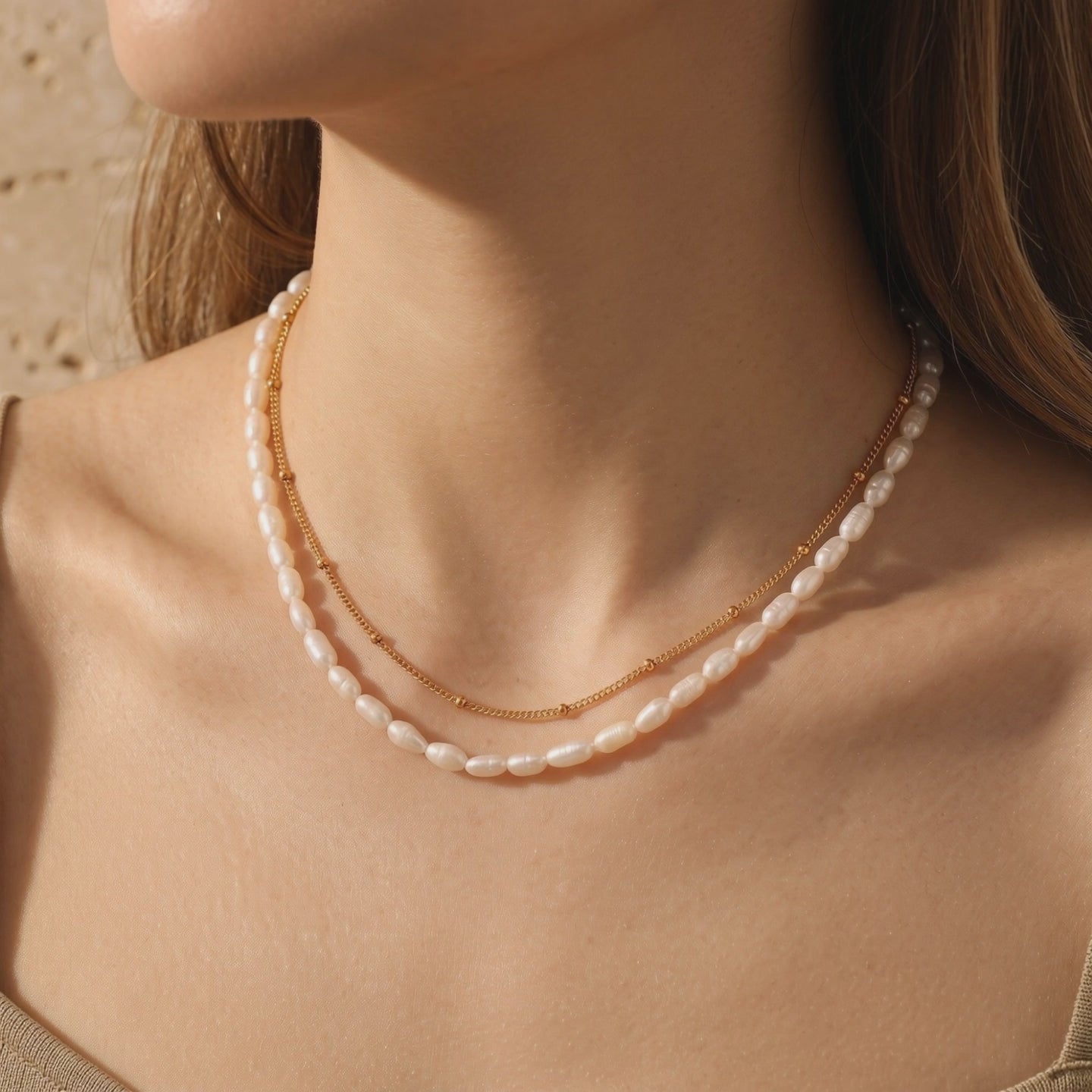Model wearing a layered necklace with a gold satellite chain and freshwater rice pearls.