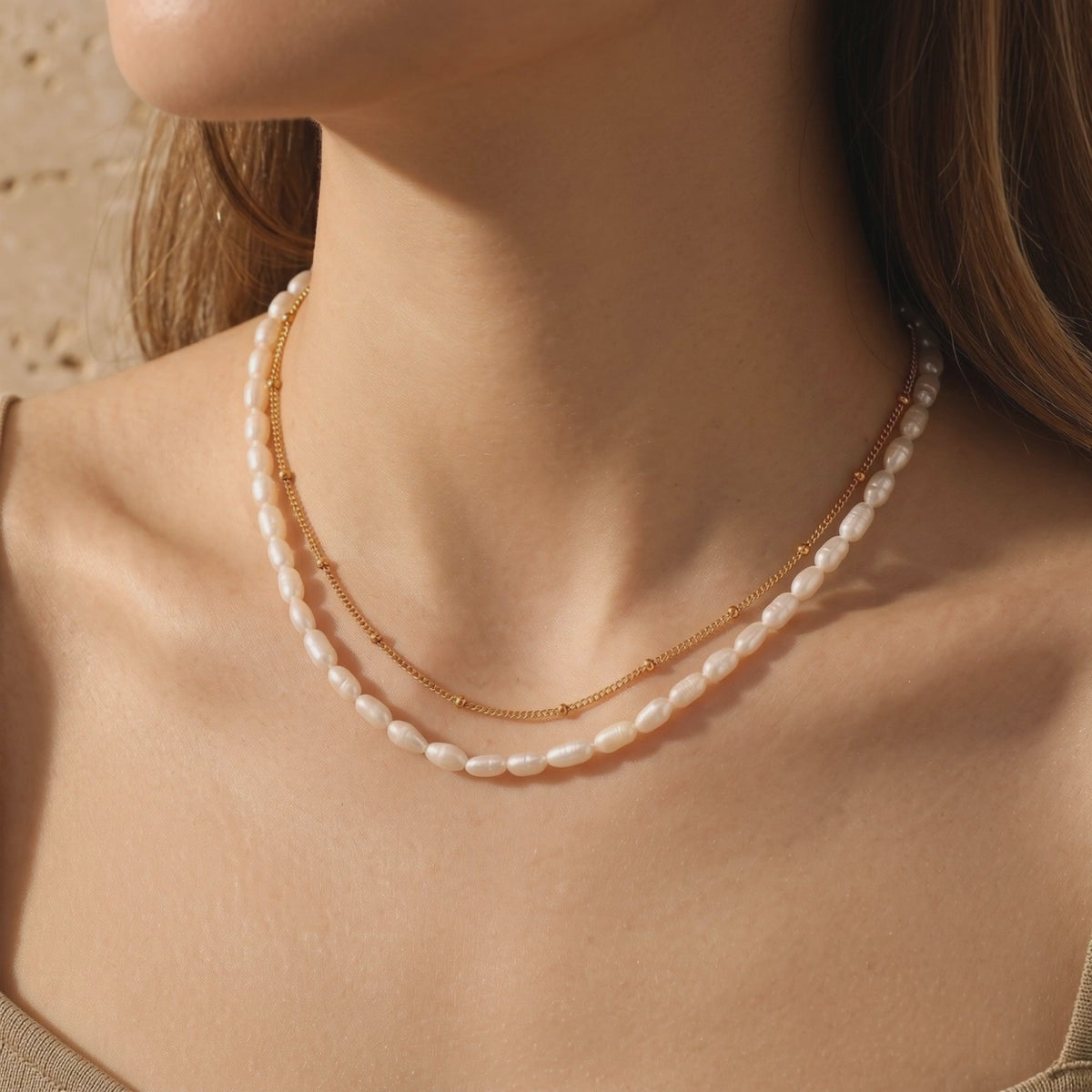 Model wearing a layered necklace with a gold satellite chain and freshwater rice pearls.