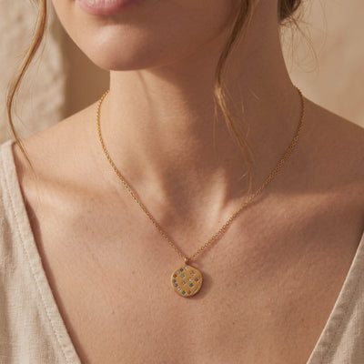 Woman wearing a gold-toned necklace with a round pendant featuring colorful inset stones.