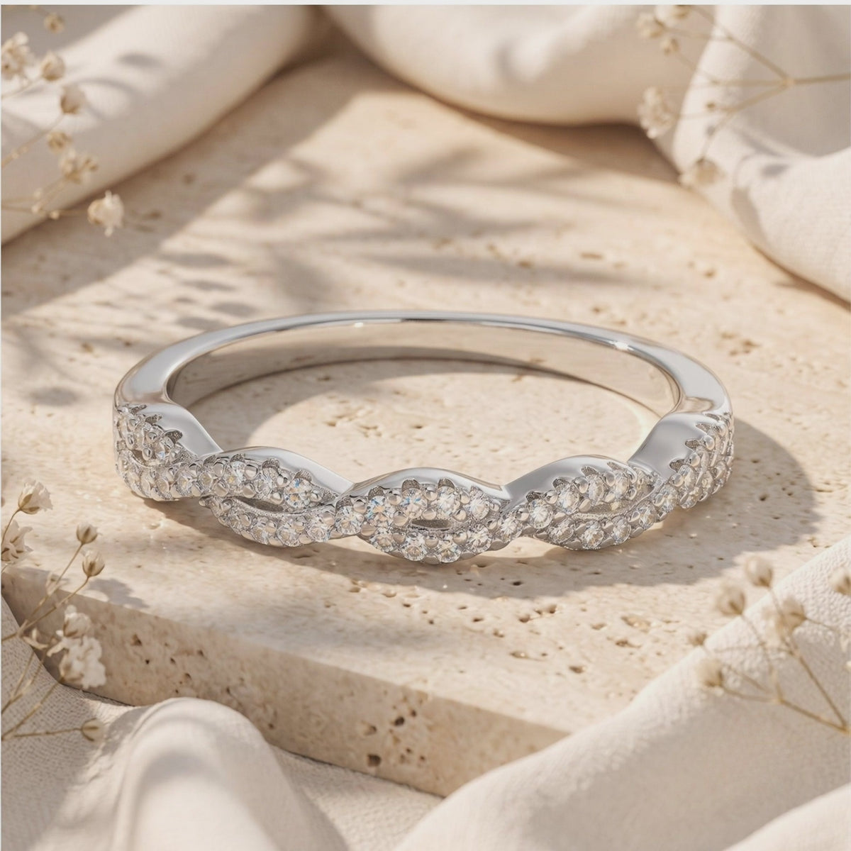 Silver twisted eternity ring with clear pavé stones resting on a textured stone block in warm sunlight.