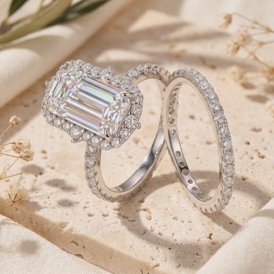 Silver-tone emerald-cut halo ring and matching pavé eternity band displayed on a textured stone surface.