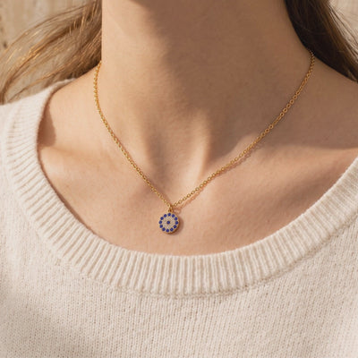 Gold-toned chain necklace worn at the neck, with a round blue-and-white pavé pendant over a cream ribbed sweater.