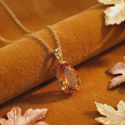 Close-up of the pear-cut simulated topaz pendant and solid gold chain resting on warm velvet.