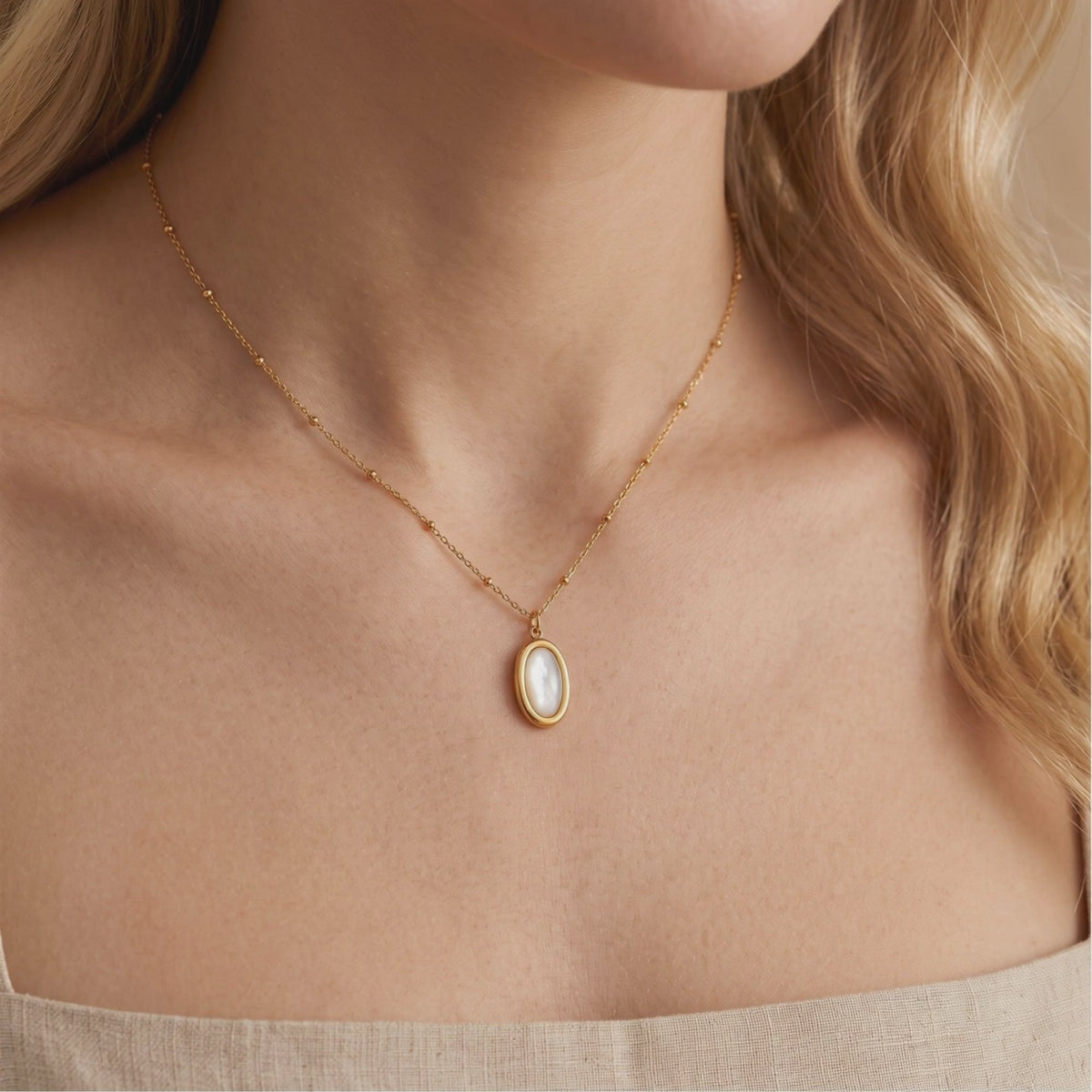 Gold satellite chain necklace with an oval mother-of-pearl pendant, shown worn on a model.
