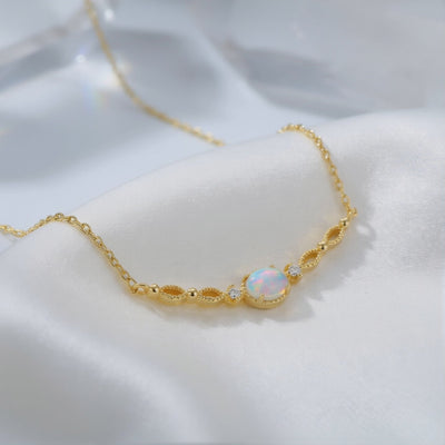 Detailed view of a solid gold white opal pendant and chain resting on white satin.