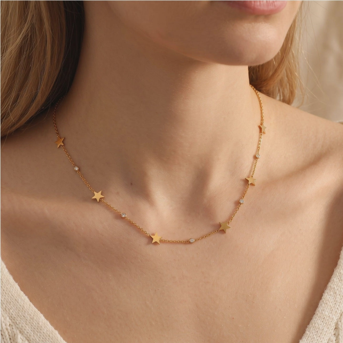 Model wearing a gold-tone necklace with star charms and round simulated diamond accents along her collarbone.