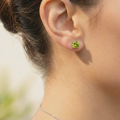 Model wearing a round yellow-green simulated peridot stud earring in a solid gold four-prong setting.