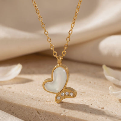 Close-up of a gold-tone butterfly pendant with mother-of-pearl inlay and four clear accent stones.