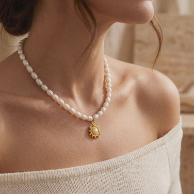 Model wearing a pearl strand necklace with a gold-tone sunburst pendant and center pearl.