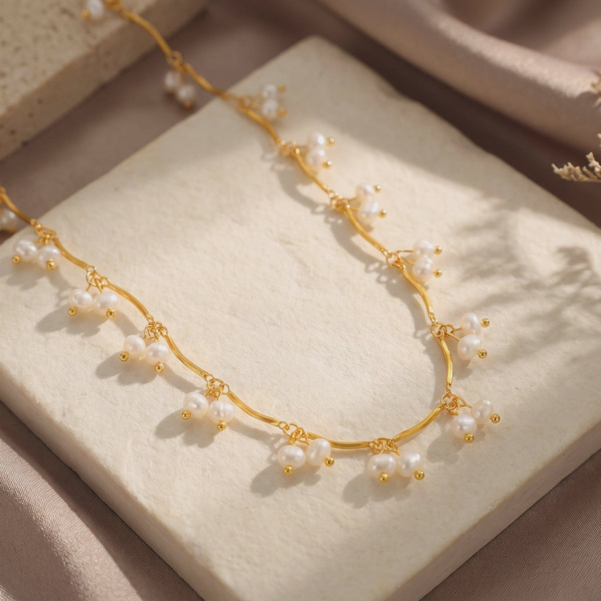 Gold-tone wavy necklace with dangling clusters of small white pearls displayed on a cream textured slab.