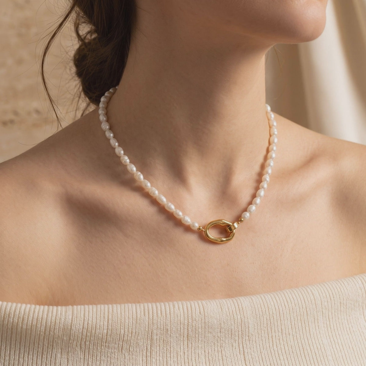 Model wearing a white rice pearl necklace with a gold-tone organic loop clasp resting at the collarbone.