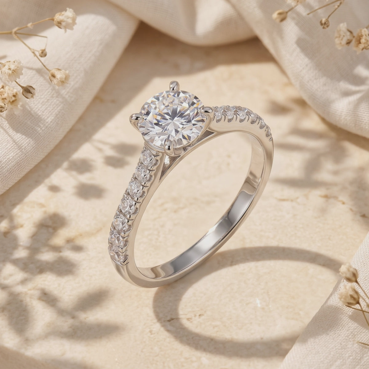 Silver solitaire ring with a round clear center stone and pavé shoulders standing on a beige textured surface.