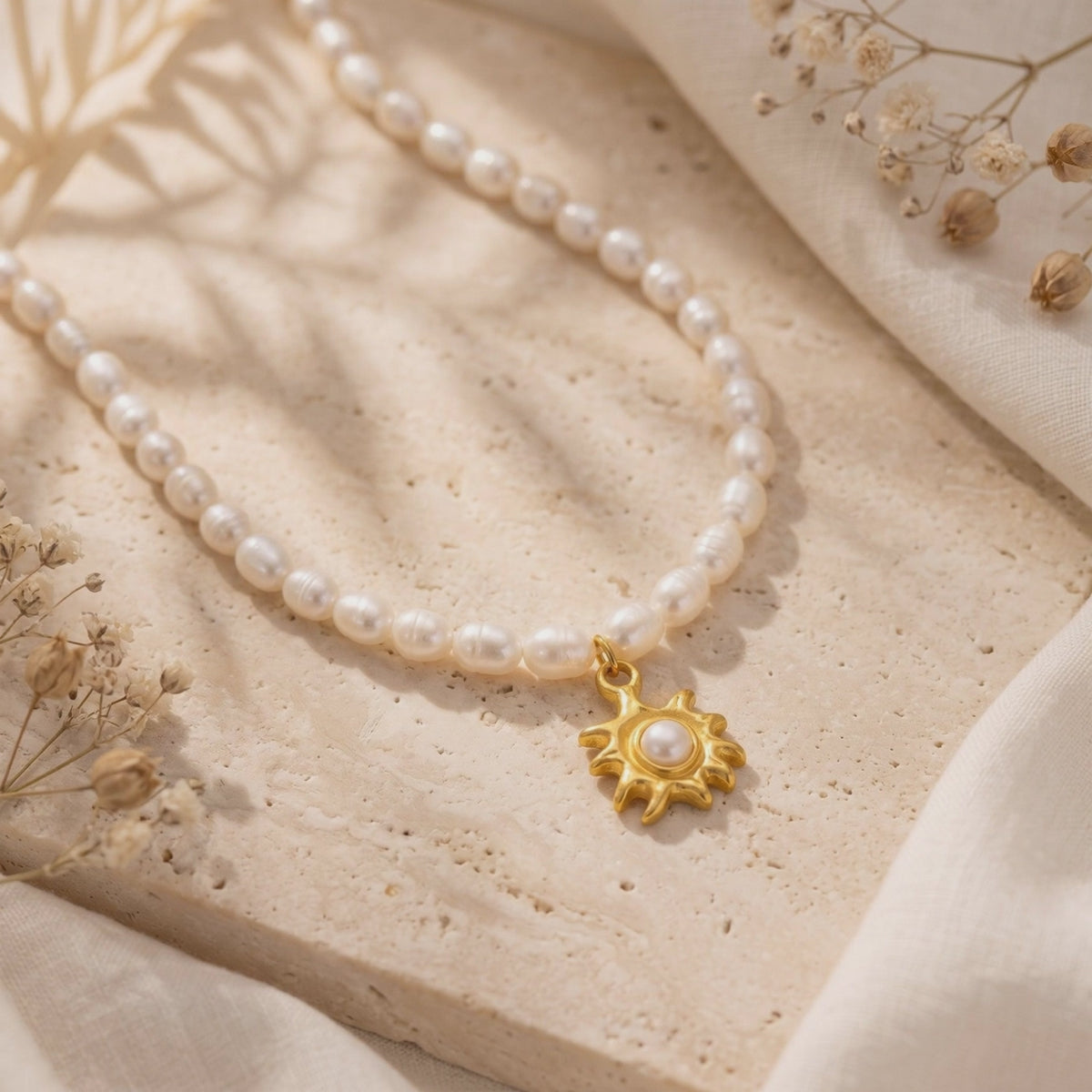 Pearl necklace arranged on a beige stone slab, with a gold-tone sunburst pendant and center pearl.