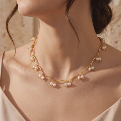 Model wearing a gold-tone wavy necklace with dangling clusters of small white pearls around her neck.