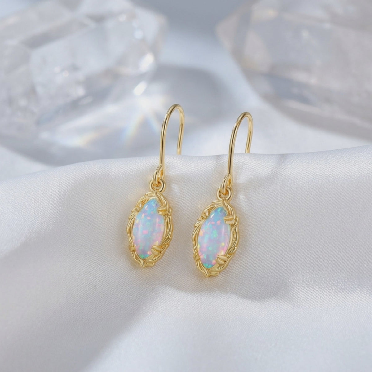 Pair of solid gold drop earrings with mariquesa-cut iridescent opals displayed on white satin.
