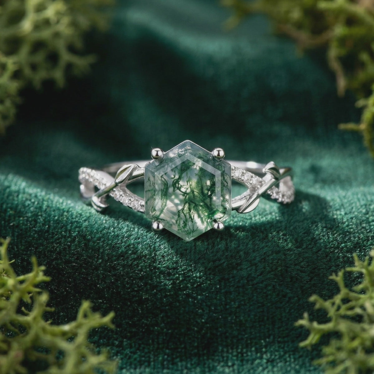 Close-up of a solid gold (white gold) hexagon moss agate ring with moissanite accents resting on green velvet.