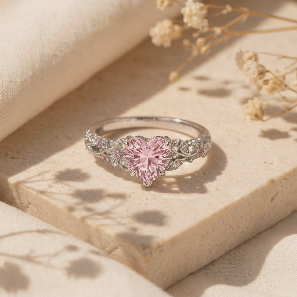 Close-up view of The Rosalique Ring, a solid gold ring with a heart-shaped pink VVS Moissanite centerpiece and floral filigree band, resting on a stone surface.