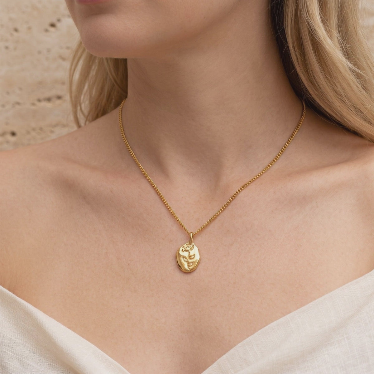 Model wearing a gold-tone necklace with a twisted chain and oval pendant etched with a rose motif.