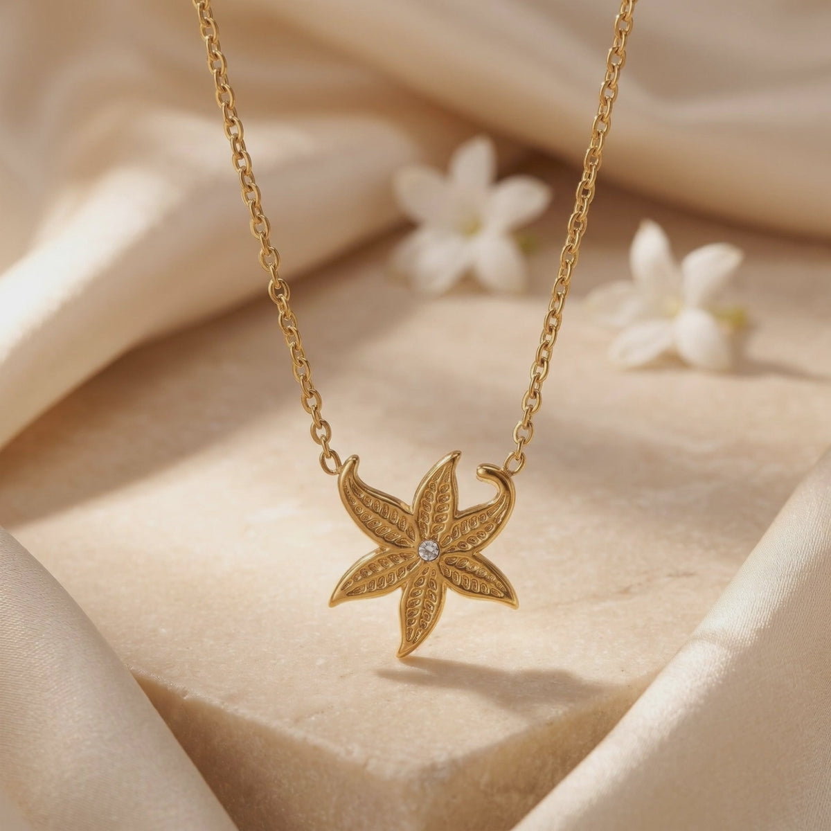 Close-up of a detailed gold-tone starfish pendant with a central clear stone over a cream display block.