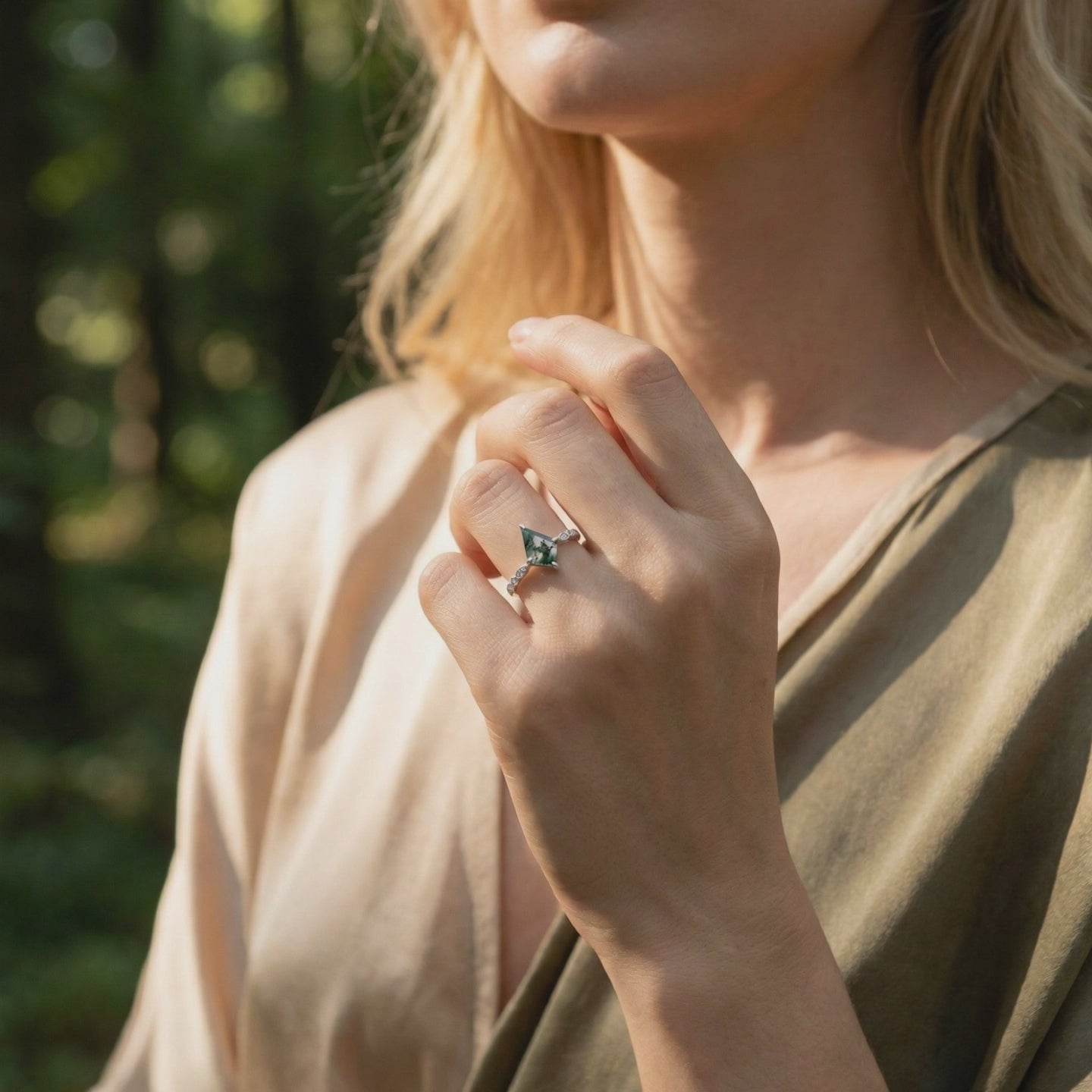 Kite cut natural moss agate ring in solid white gold worn on a hand against a blurred forest background.