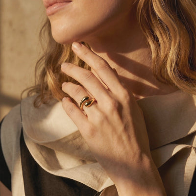 A solid gold open bypass ring with rounded ends, worn on a hand beside a person's chin.