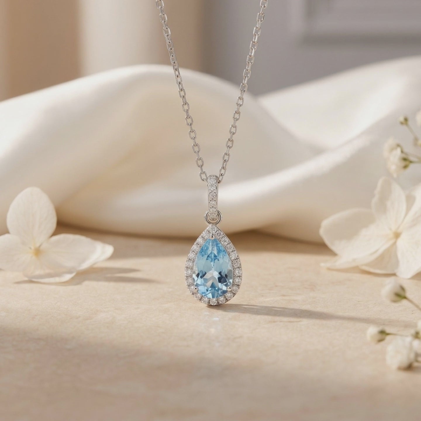 Aquamarine halo pendant necklace in solid gold near white flowers.