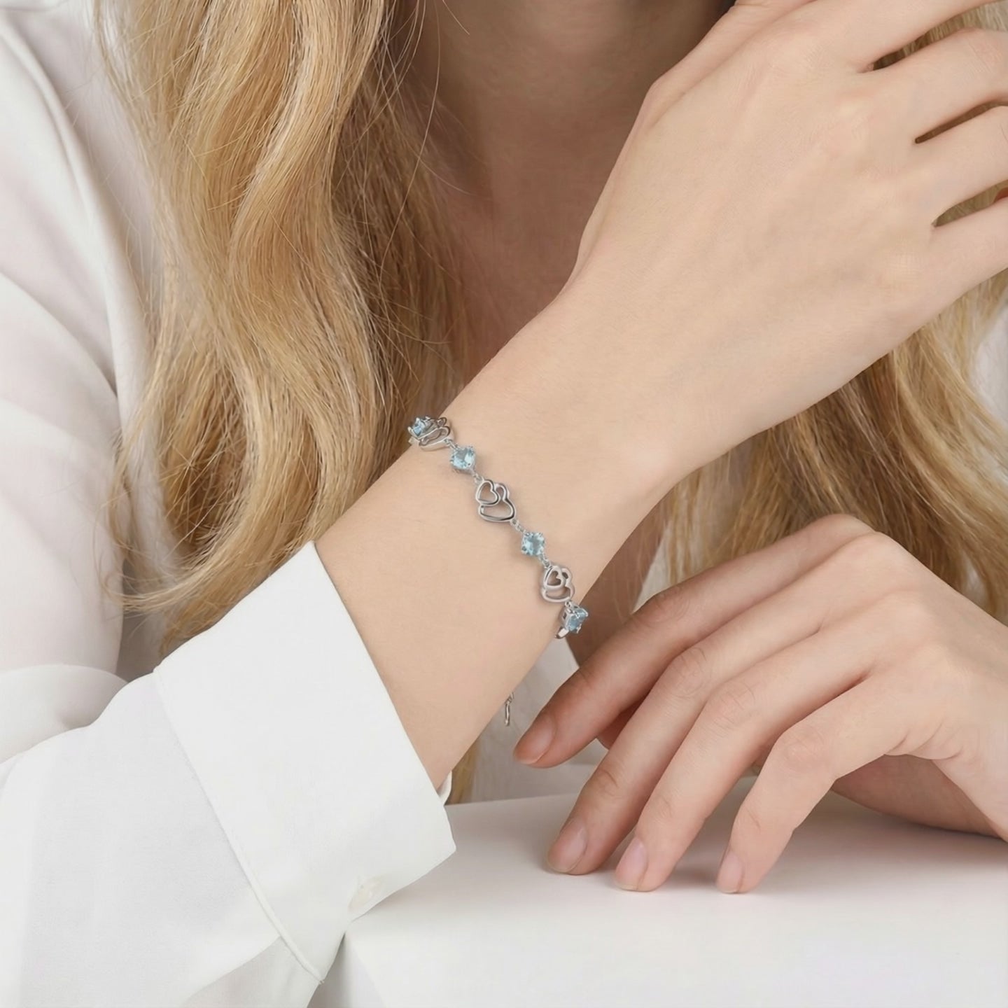 The Caelia Heart solid gold bracelet featuring an interlocking heart motif and precision-cut simulated aquamarine stones.