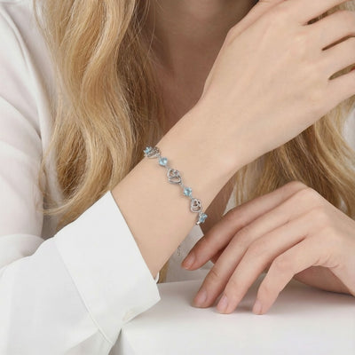 The Caelia Heart solid gold bracelet featuring an interlocking heart motif and precision-cut simulated aquamarine stones.
