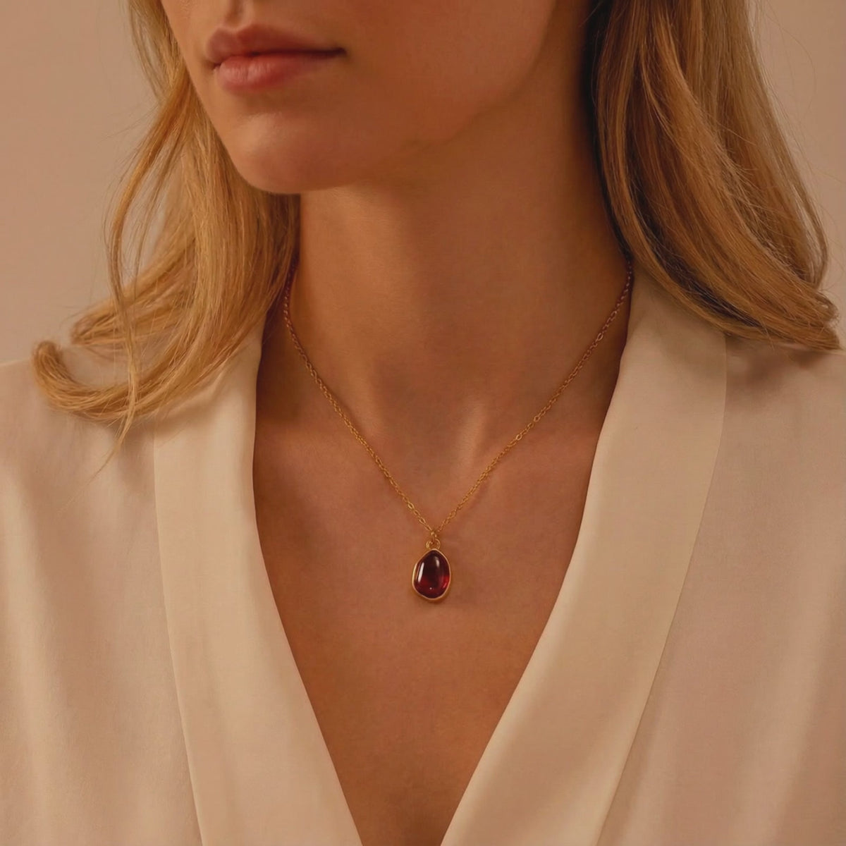 Solid gold necklace with a deep red teardrop simulated garnet pendant worn at a woman's neck.