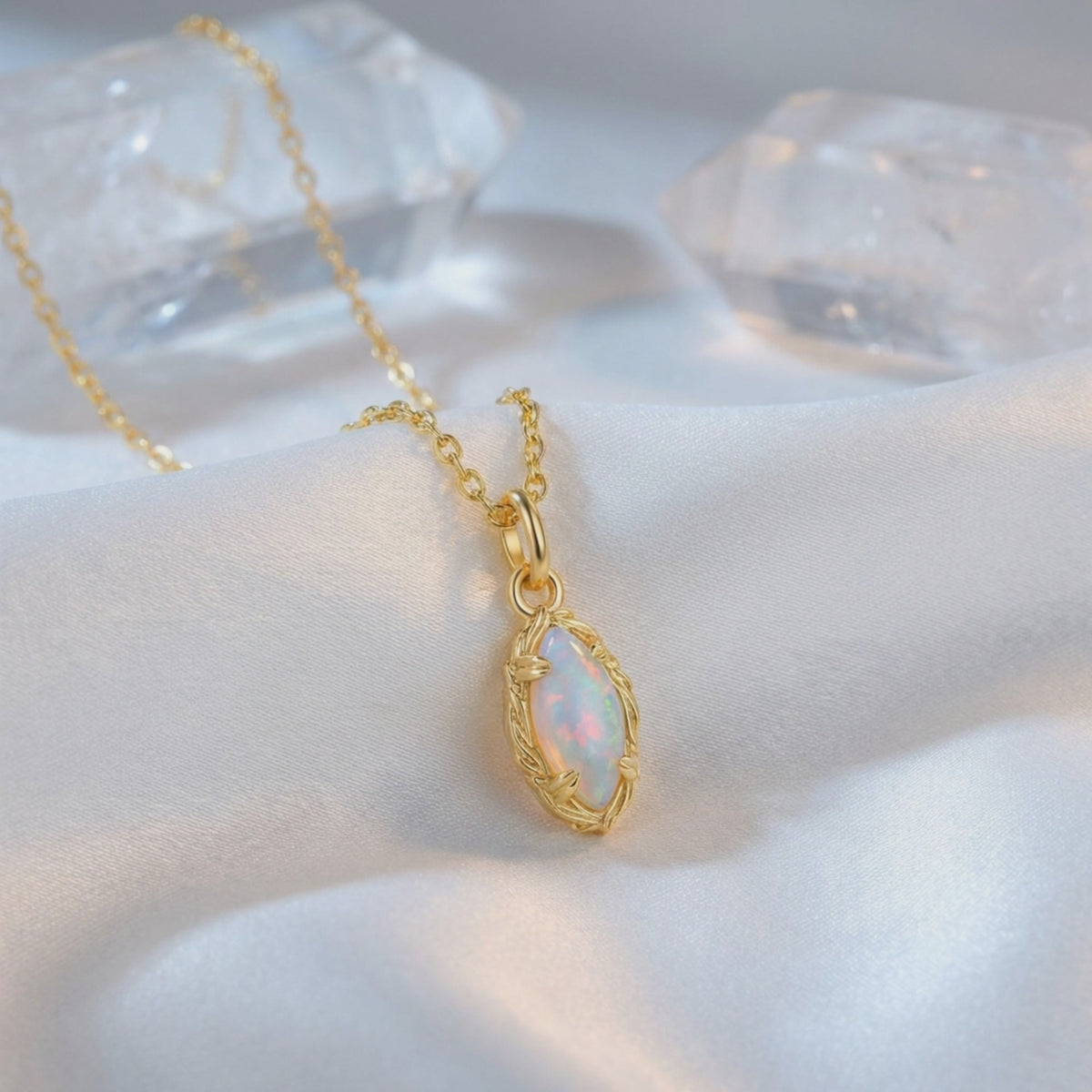 Close-up of a marquise opal pendant necklace in solid gold with a textured frame and chain on white fabric.