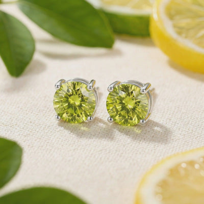 Pair of round yellow-green simulated peridot stud earrings in solid gold settings on a textured beige surface.