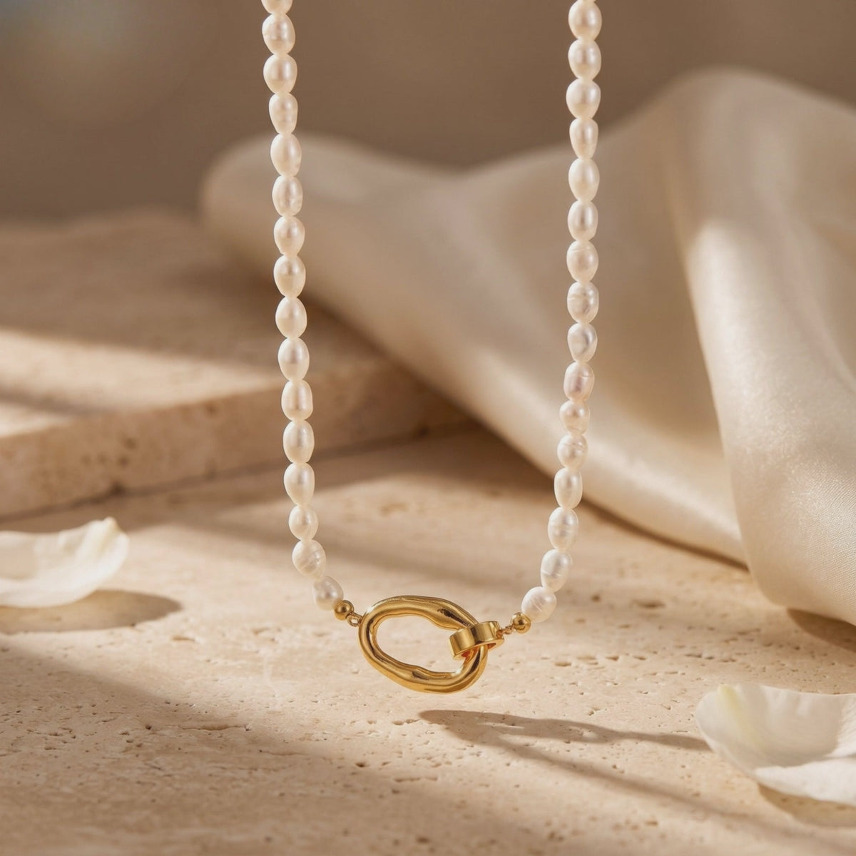 White rice pearl necklace displayed hanging above a warm textured surface, with its gold-tone loop clasp at the bottom.