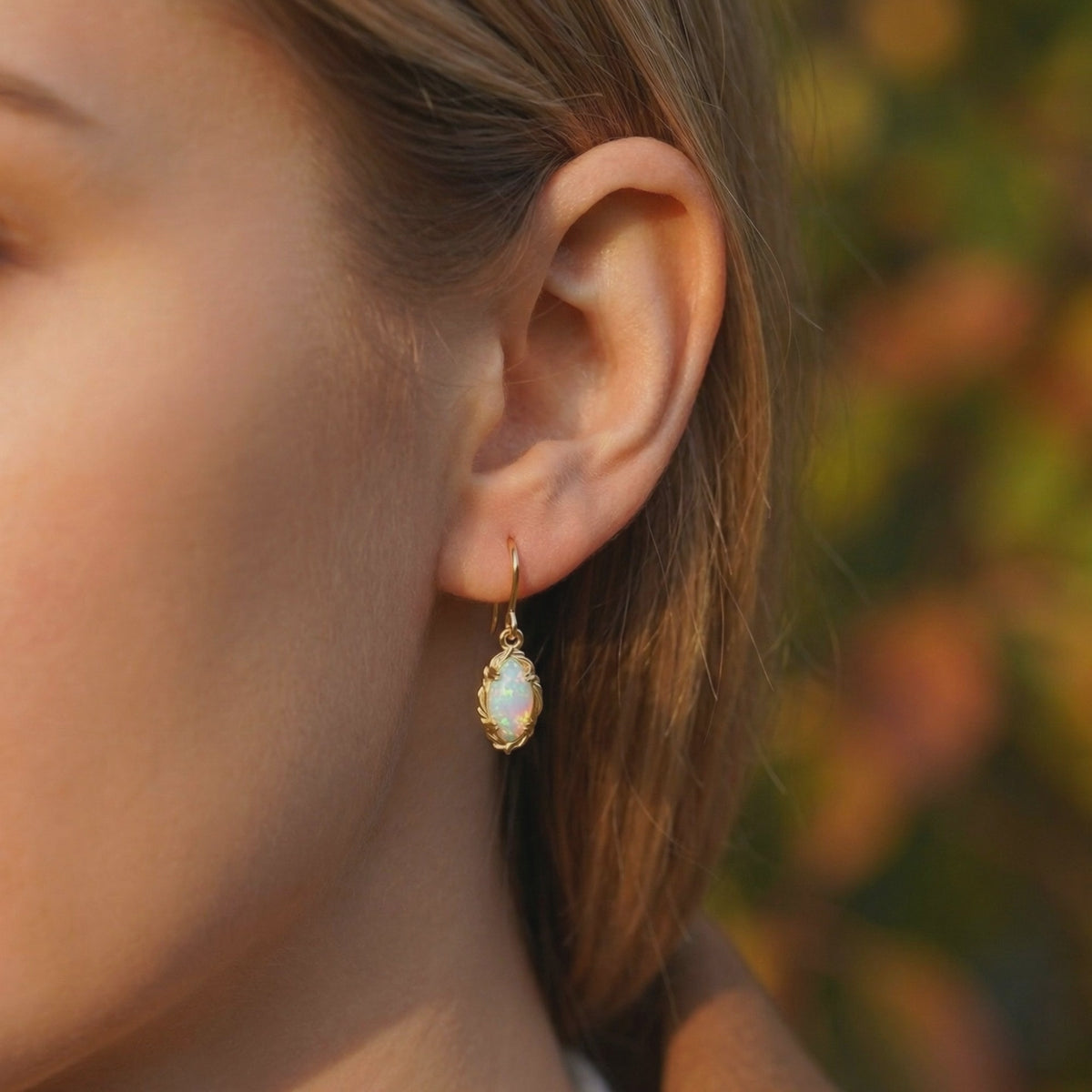 Close-up of a woman wearing one solid gold drop earring with an iridescent mariquesa-cut opal.