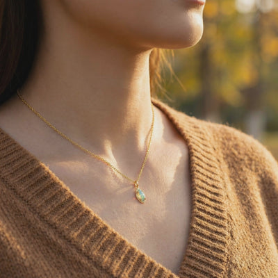 Marquise opal pendant necklace in solid gold worn over a brown knit V-neck sweater.