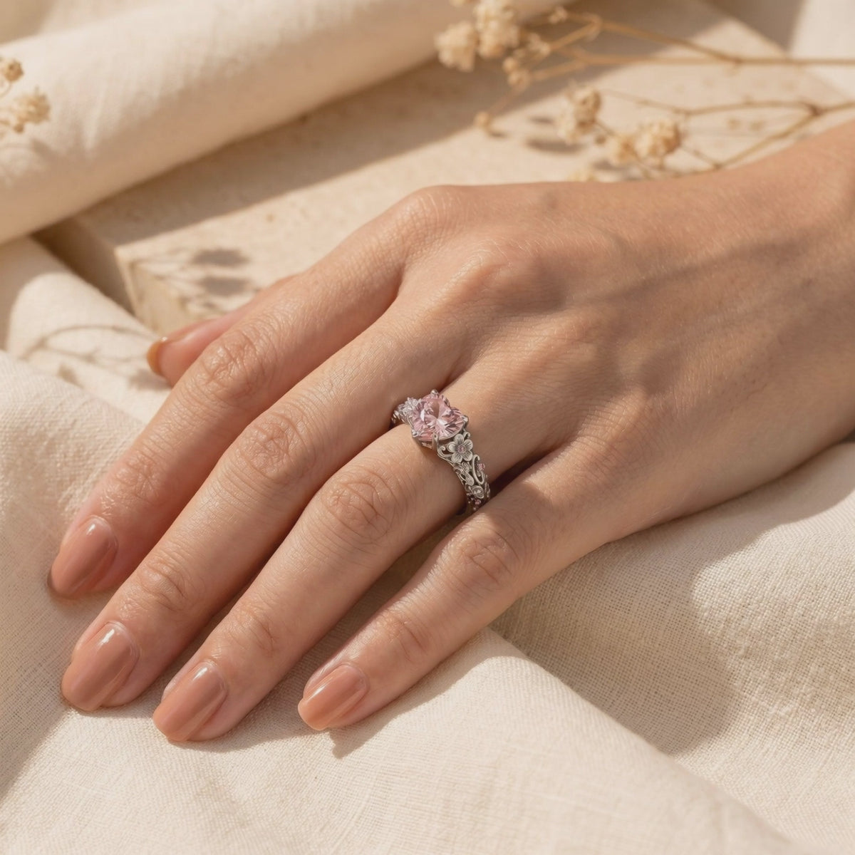 The Rosalique Ring, a solid gold ring with a heart-shaped pink VVS Moissanite centerpiece and floral band detailing, worn on a hand.