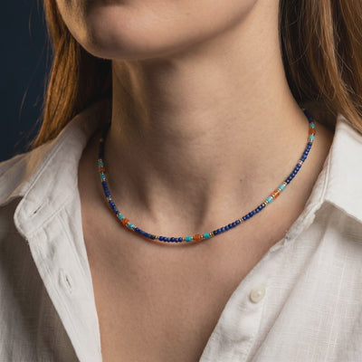 Solid gold lapis lazuli bead necklace worn at the neck over a white shirt.