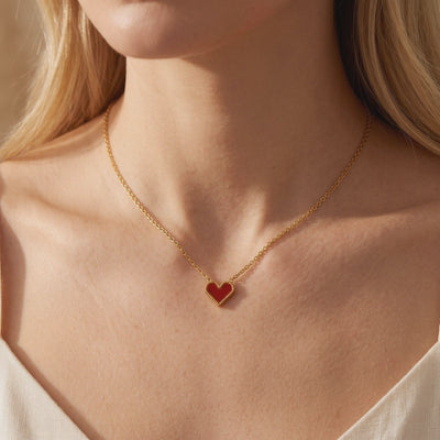 Model wearing a gold chain necklace with a red heart pendant framed by a beaded gold border.
