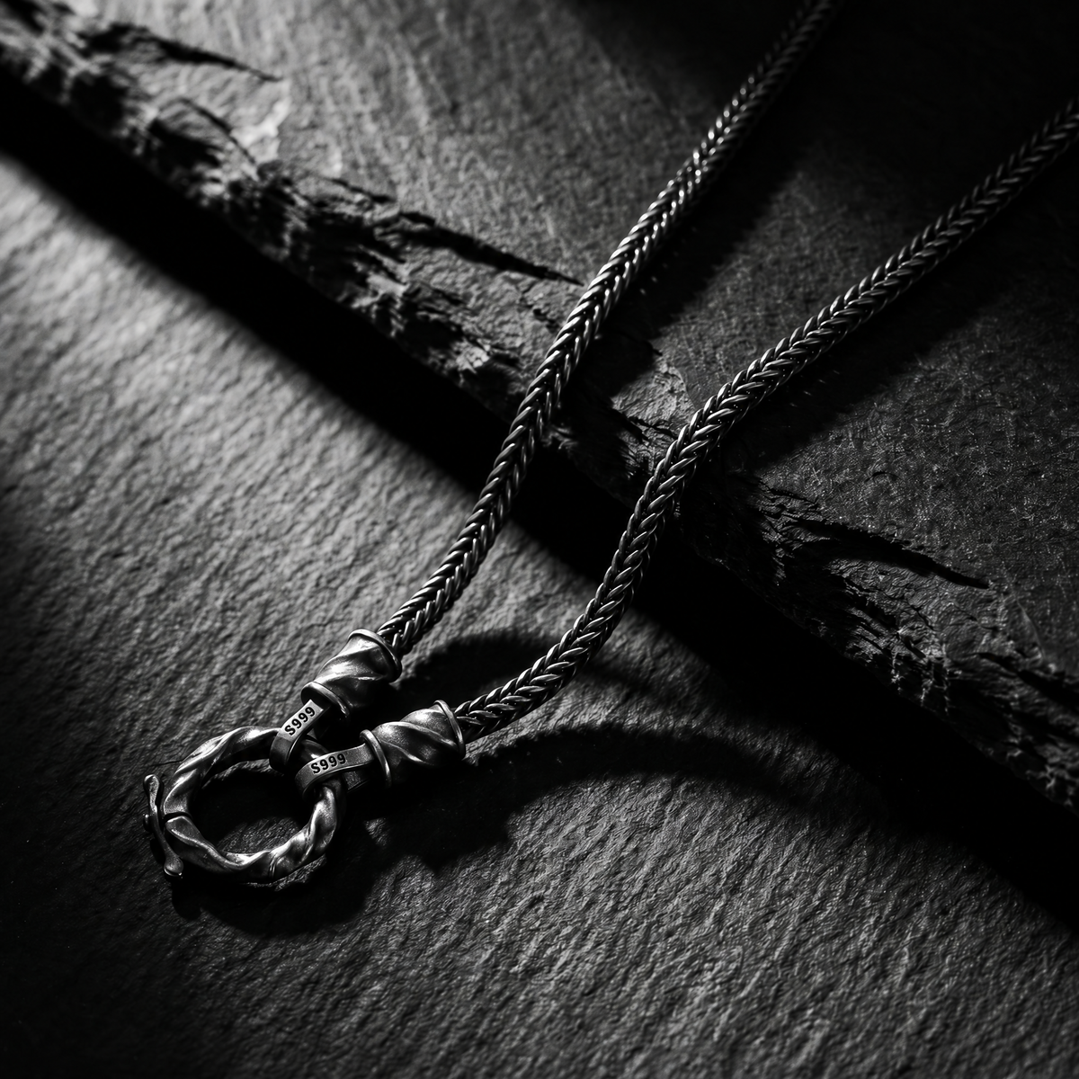 Silver twisted ring necklace and braided chain resting on dark slate stone.
