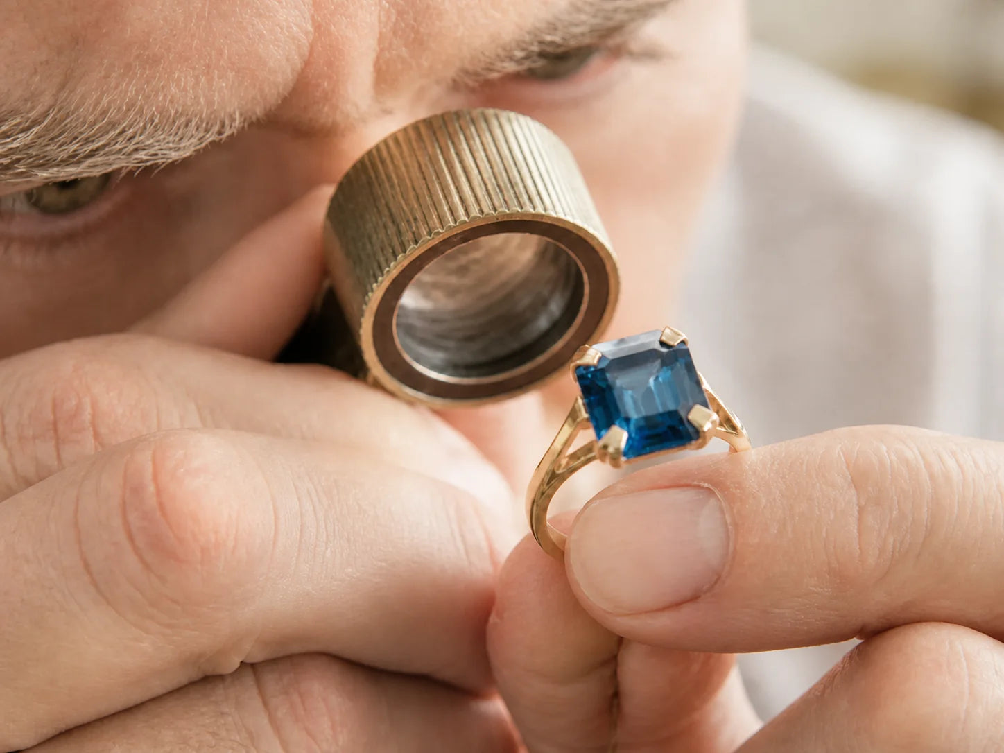 Jeweler inspecting a blue gemstone ring through a loupe