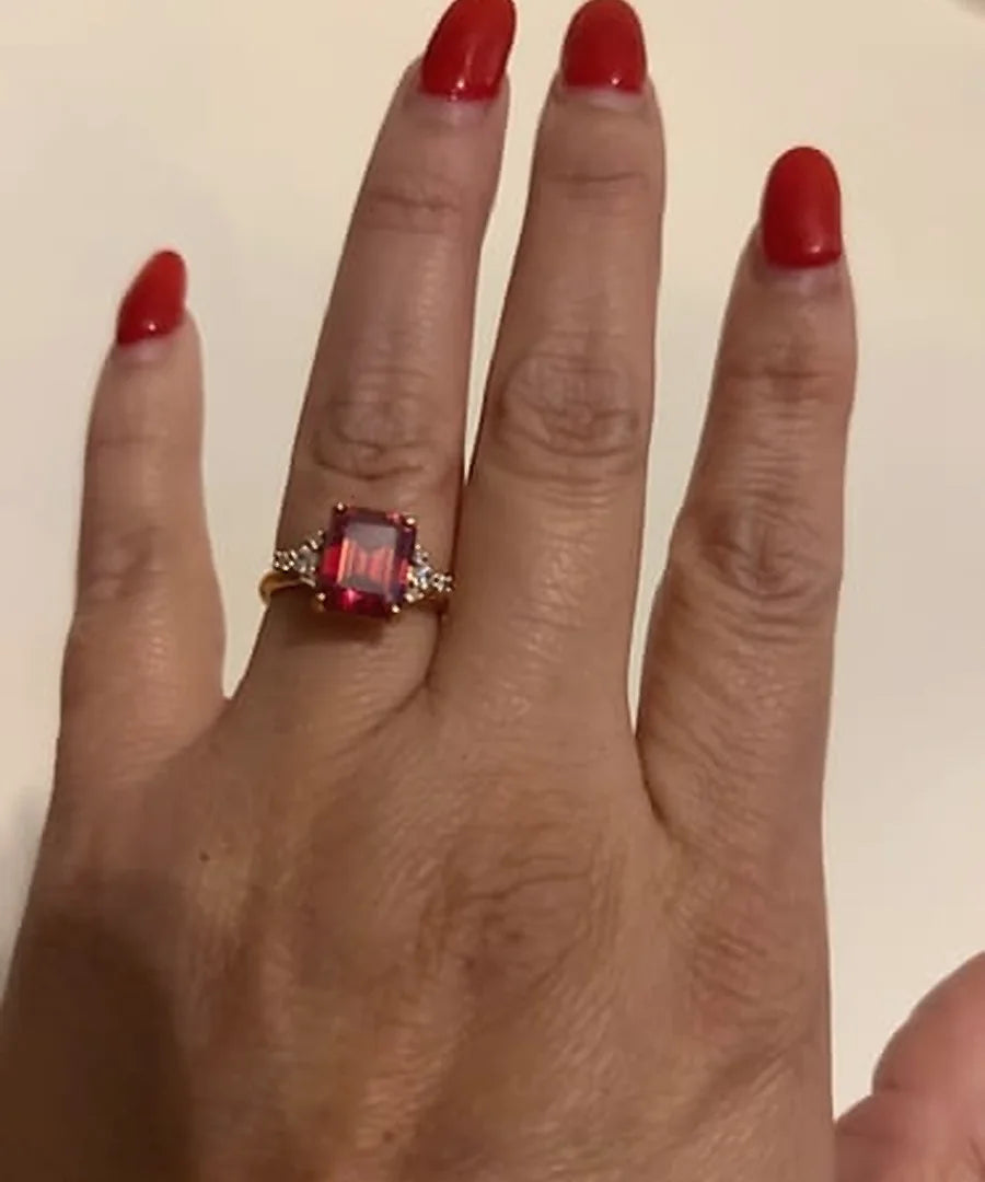 Red emerald-cut engagement ring worn on a customer's hand